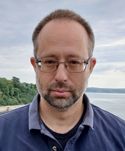 a man's face and shoulders, wearing a blue shirt and glasses