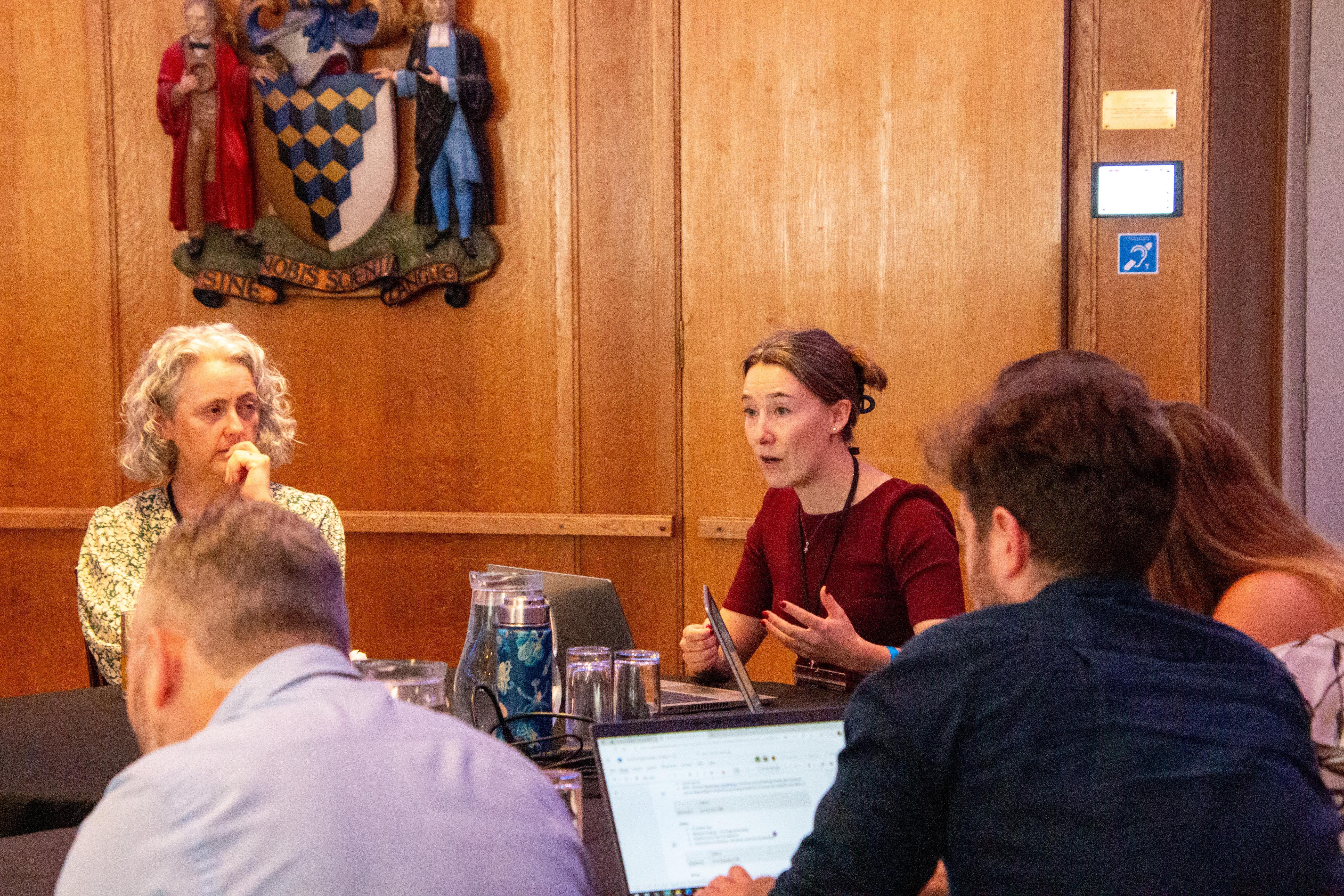a woman engaging in discussion around a table with multiple people listening
