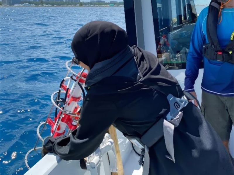 a woman wearing a lifejacket is lowering a piece of scientific equipment into the ocean, during a training exercise on a boat