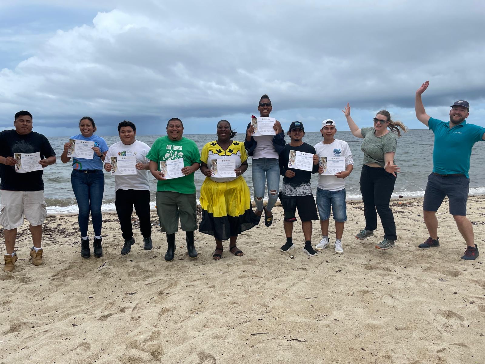 a group of people holding certificates in a row, jumping with joy on a beach