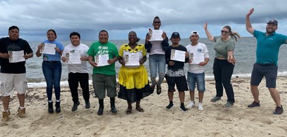 a group of people holding certificates in a row, jumping with joy on a beach