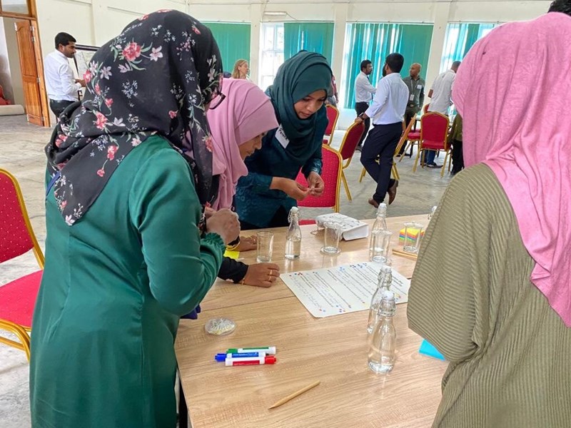 a group of woman wearing headscarves leaning over a table reading a piece of paper and participating in an activity. There are coloured marker pens on the table.