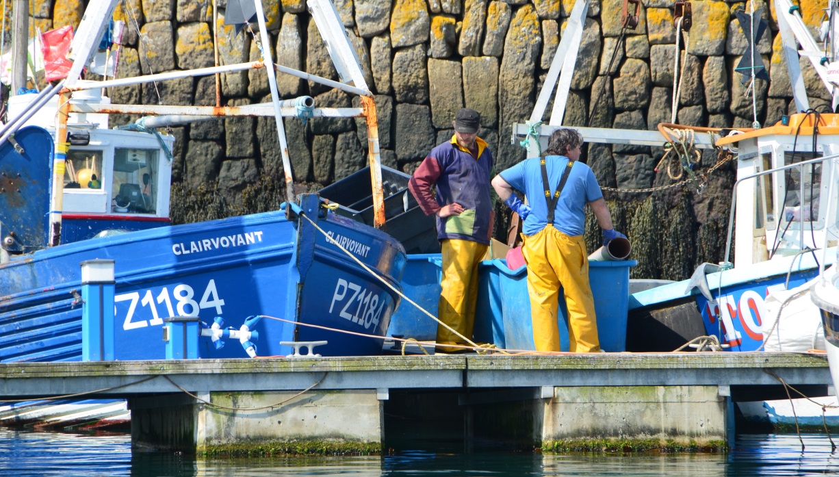 two fishermen next to boats by a rock wall