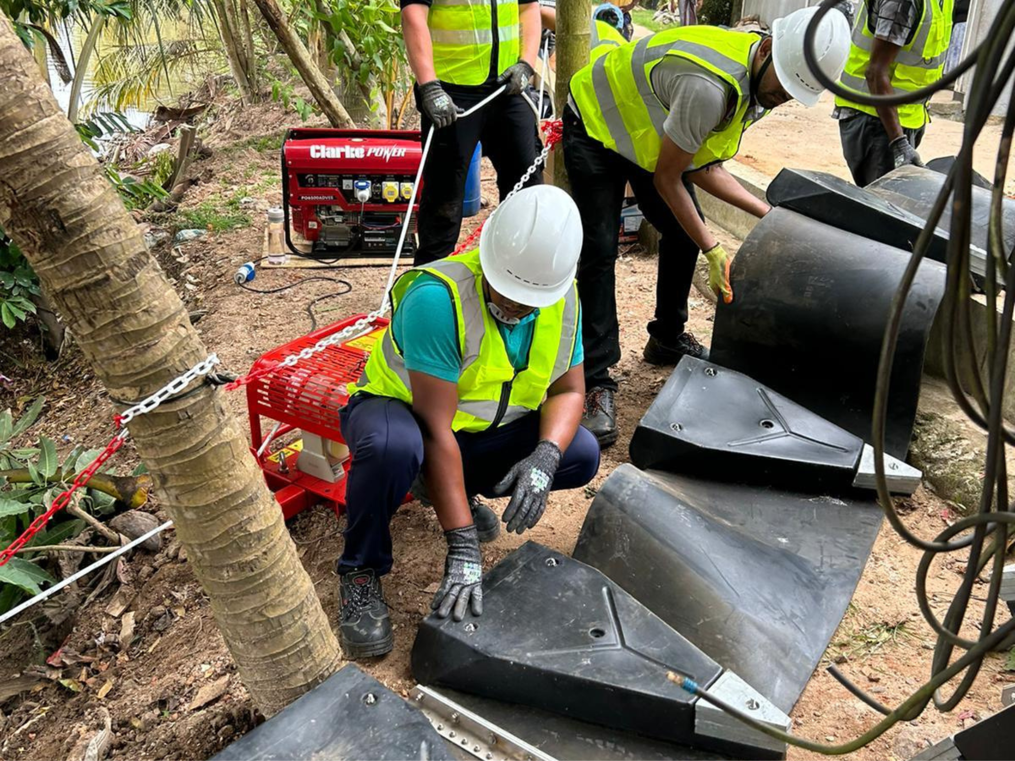 a man in hi-vis and a hard hat, and wearing other PPE, is helping to deploy a litter boom, moving it down a slope with colleagues in the background also helping