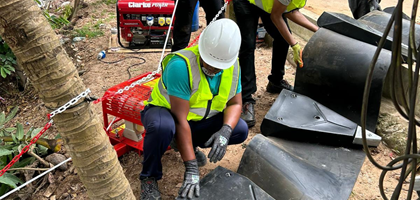 a man in hi-vis and a hard hat, and wearing other PPE, is helping to deploy a litter boom, moving it down a slope with colleagues in the background also helping