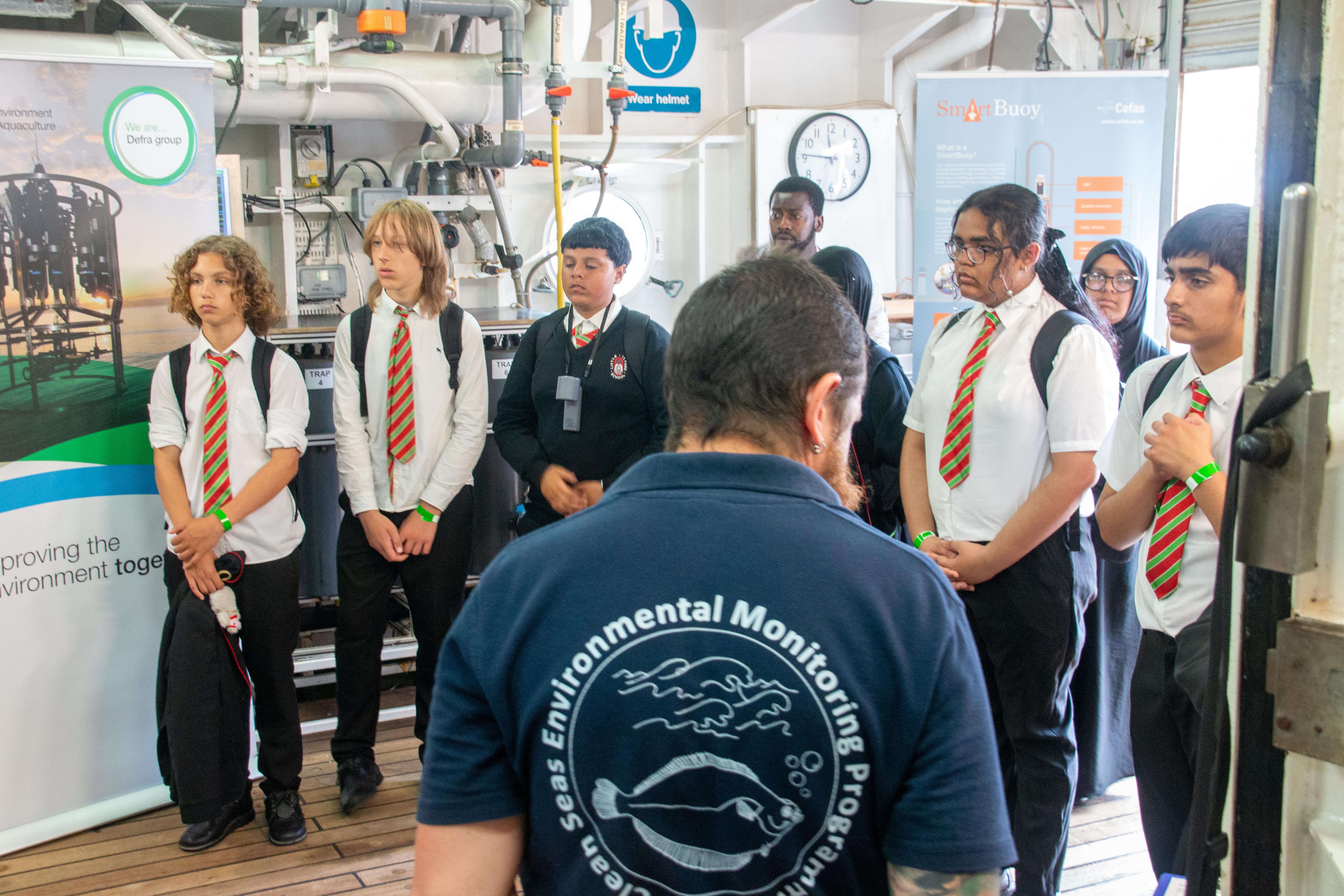 School children standing aboard the Cefas endeavour listening to a talk from staff