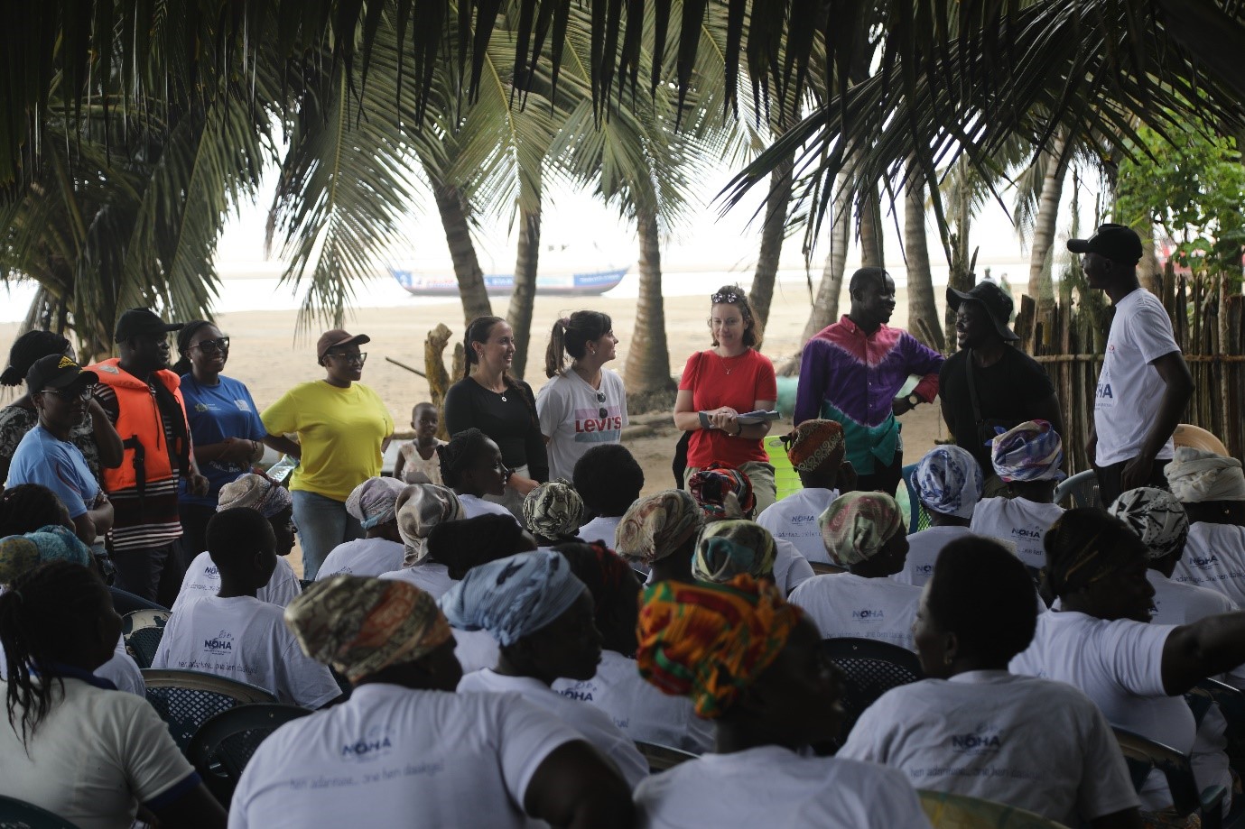 a large group of women in matching group tshirts sat down, facing a group of people standing in front of them giving a talk