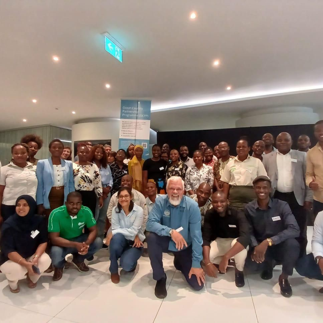 A group of people, with two rows standing, and a row in front who are kneeling, posing for a photo in font of a banner which says Ocean Country Partnership Programme (OCPP)