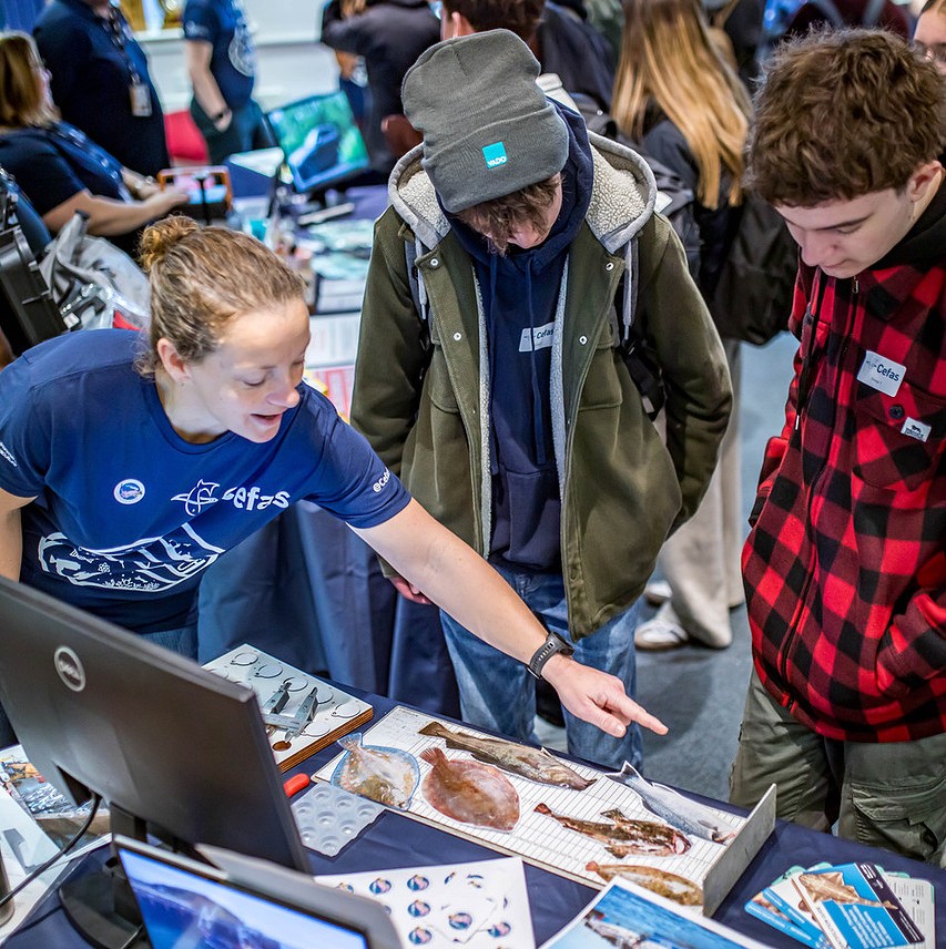 Cefas staff member pointing to fish images on a measuring board