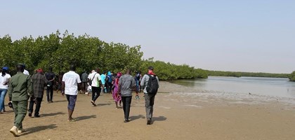 a group of people walking on a riverbank of sand alongside a river on a field trip