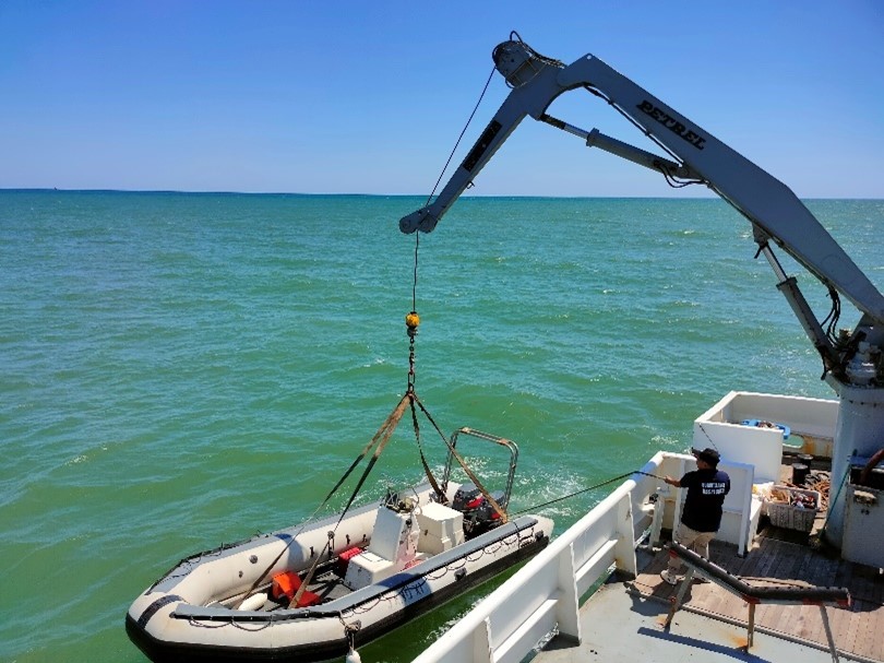a speed boat being lowered into the water from another boat