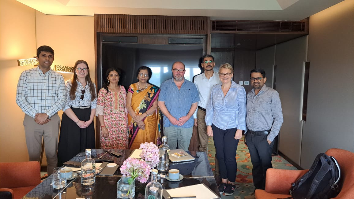 A group of people stood behind a table after a meeting, smiling and posing next to each other for a photograph