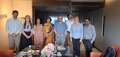 A group of people stood behind a table after a meeting, smiling and posing next to each other for a photograph