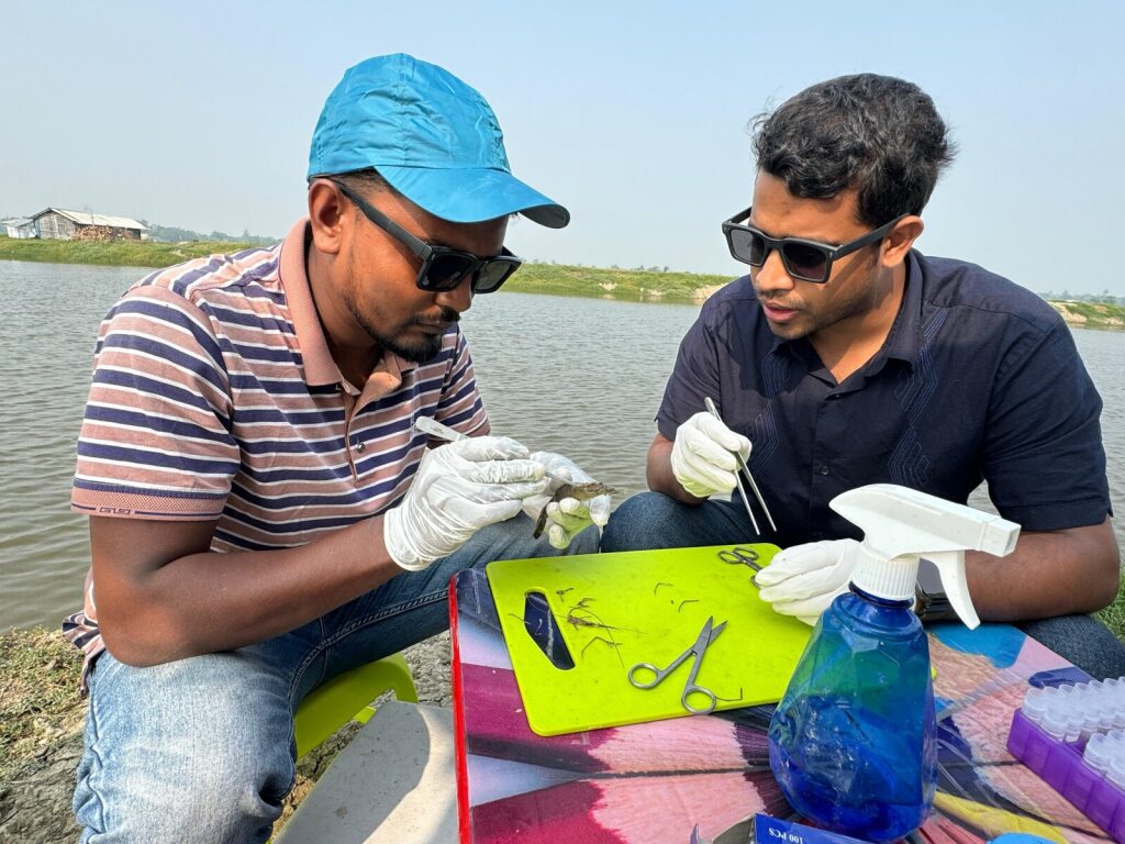 two students conducting field research with science tools next to a body of water