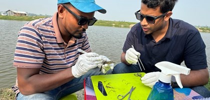 two students conducting field research with science tools next to a body of water