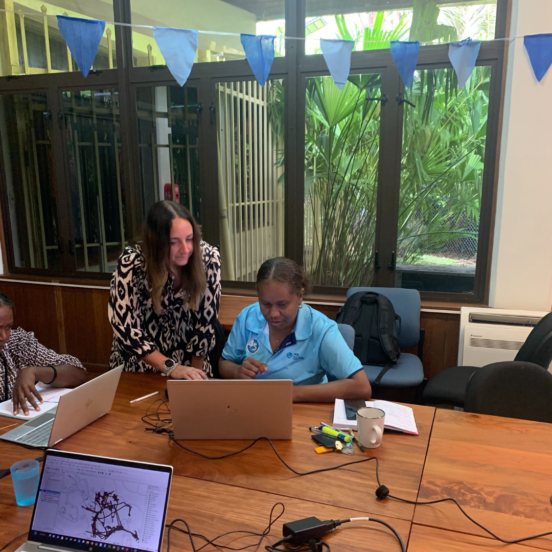 a woman in uniform is sat down in front of a laptop in an office-like setting, with another woman standing next to her and leaning over slightly whilst pointing to something on the laptop screen
