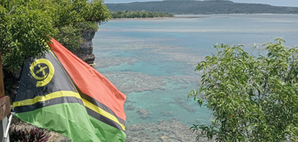 picture of the Vanuatu flag blowing in the breeze and a healthy reef behind in the ocean